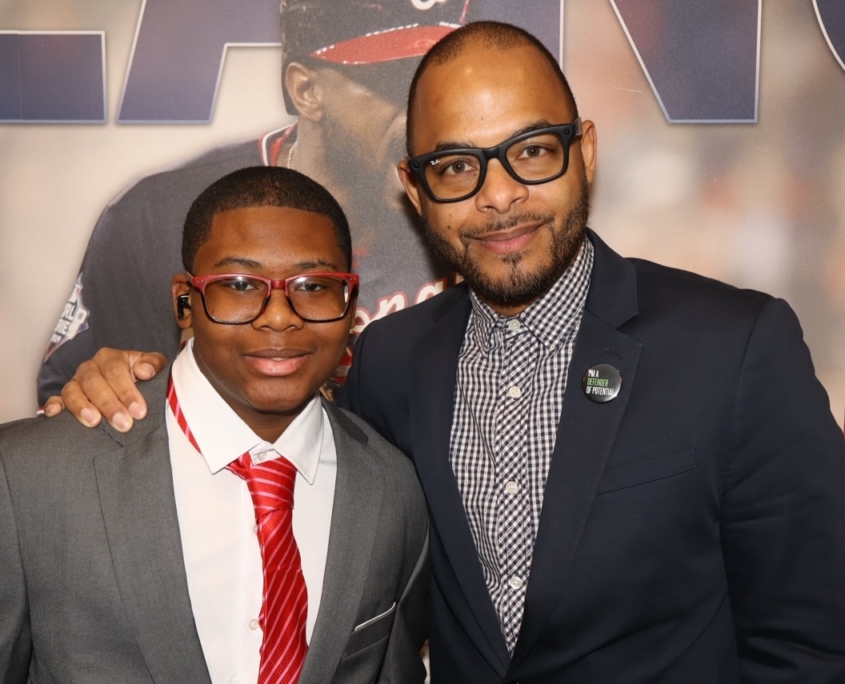 a photo of a young teenager and an adult male smiling next to eachother