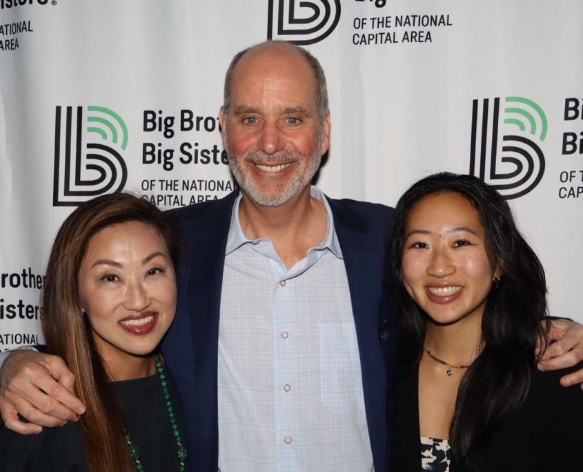 2 woman and an adult male standing in the middle smiling for a group photo